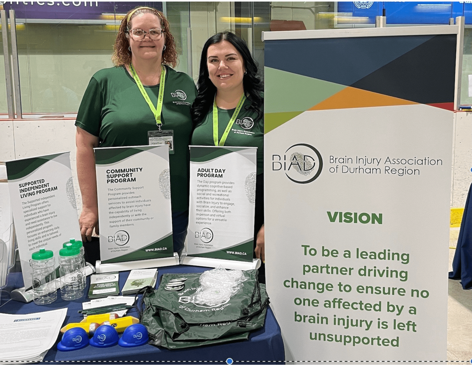 Heather and Amy standing in green BIAD shirts in front of a display table with BIAD information